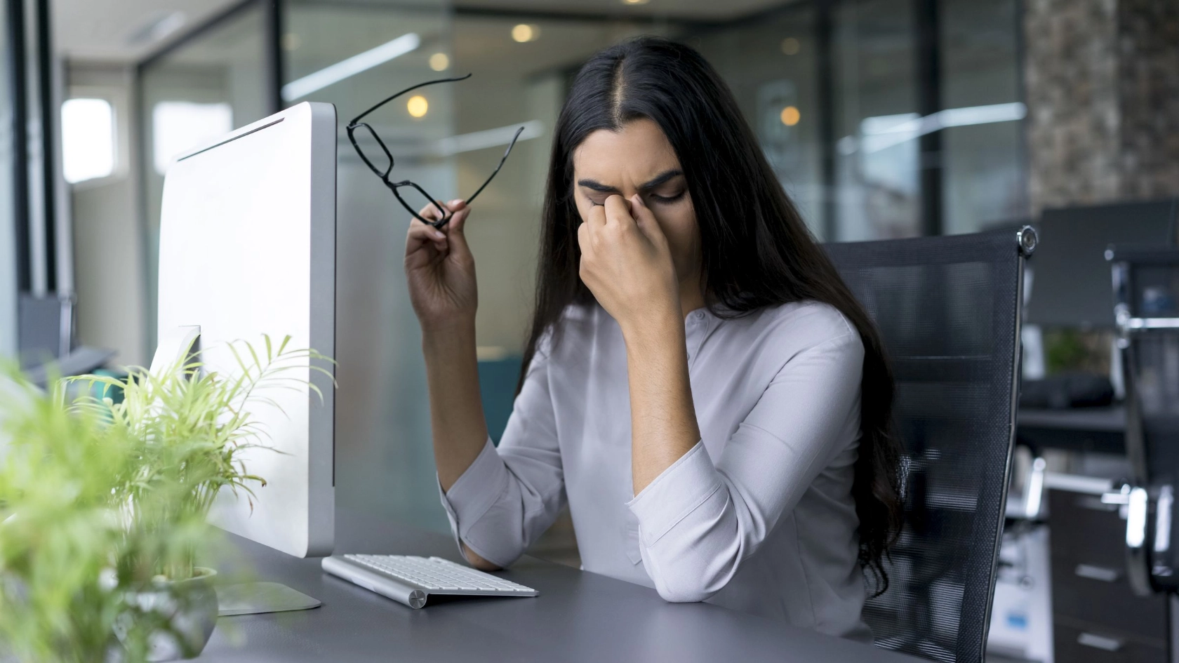 Eine junge Frau reibt sich im Büro aus Übermüdung die Augen
